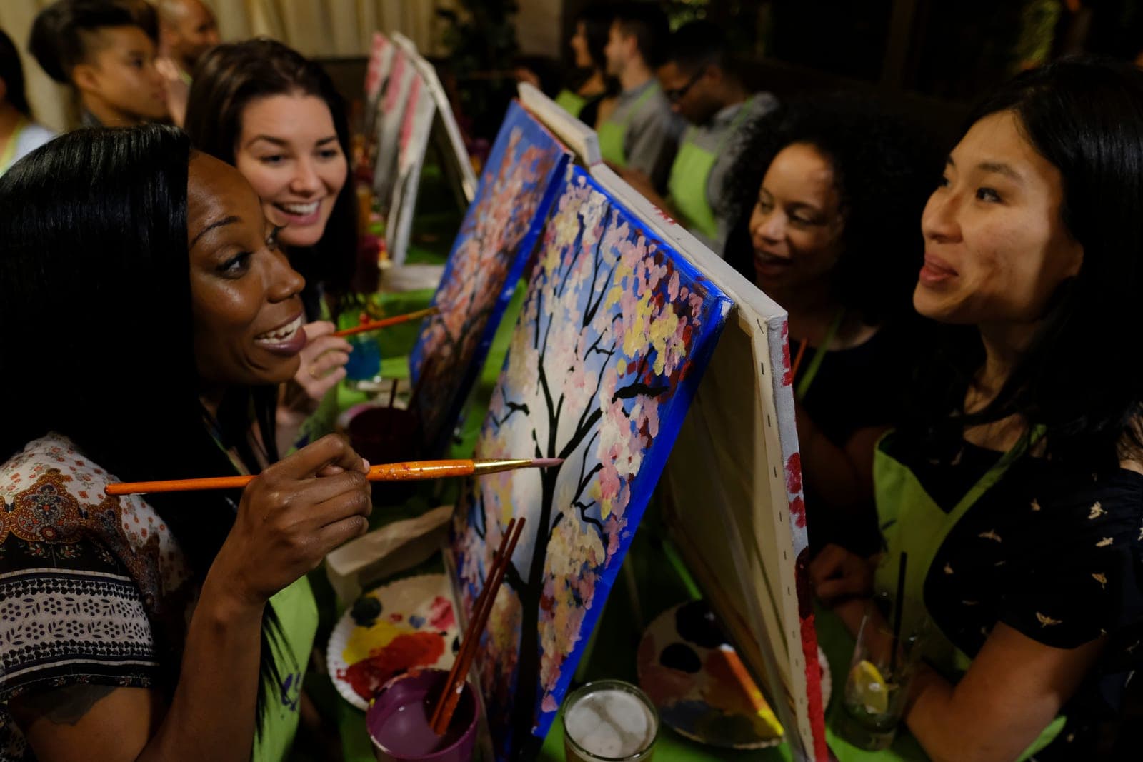 Four friends comparing their cherry blossom paintings, drinks on the table