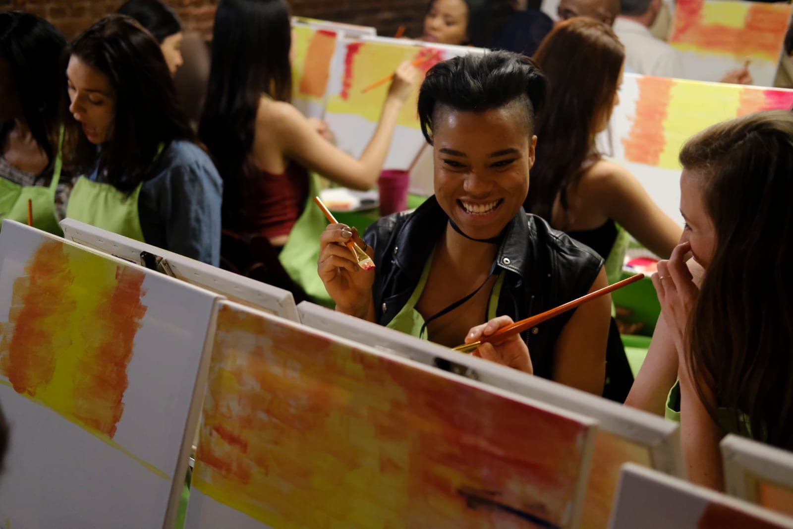 A guest laughing with a friend over their canvases at a Paint Nite event